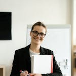 Professional woman in a classroom holding documents and smiling warmly.