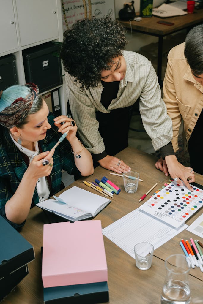 Three businesswomen collaborating over color samples in an office setting. Diversity and teamwork emphasized.